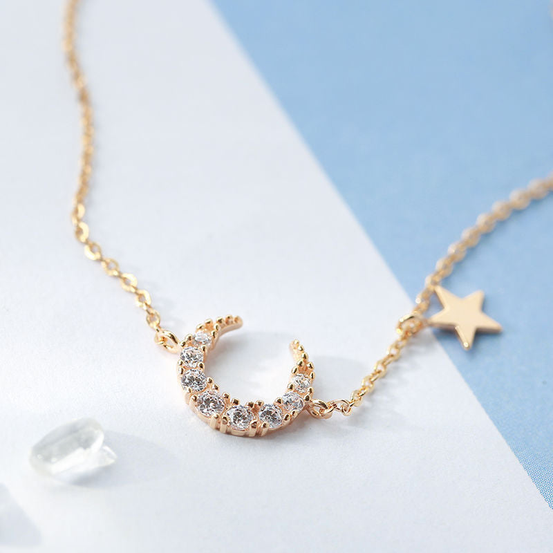 Gros plan sur un bracelet délicat en argent avec un pendentif en forme de lune sertie de cristaux et une petite étoile dorée suspendue à une chaîne fine.