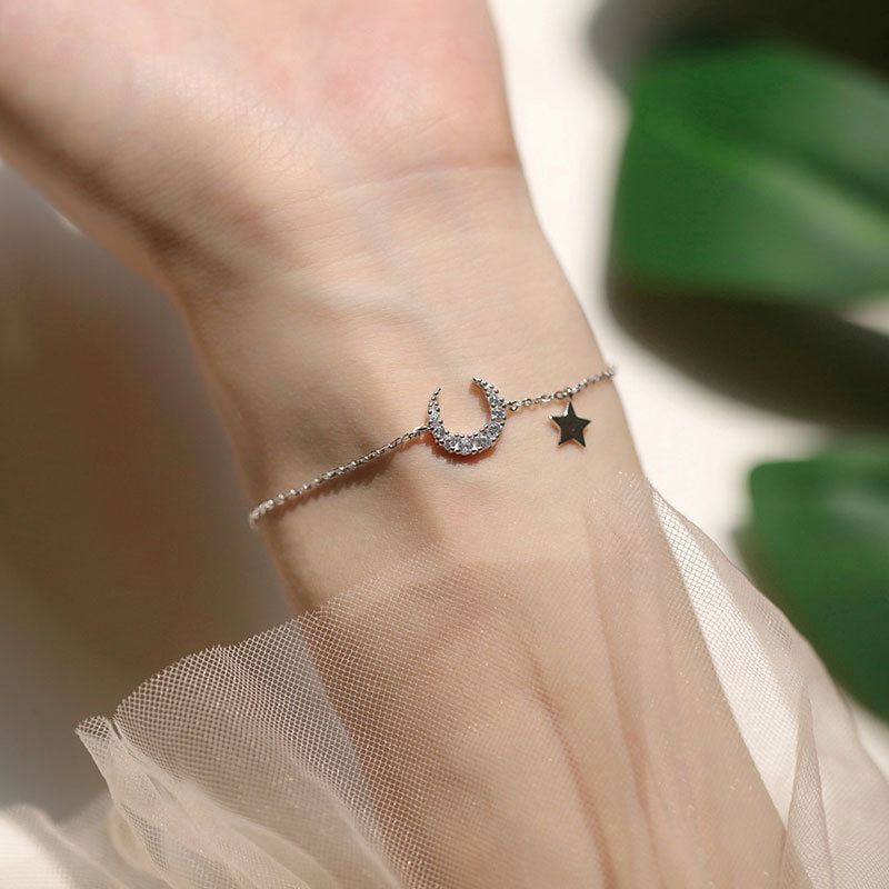 Bracelet délicat en argent avec un pendentif en forme de croissant de lune orné de zircons et une petite étoile suspendue.