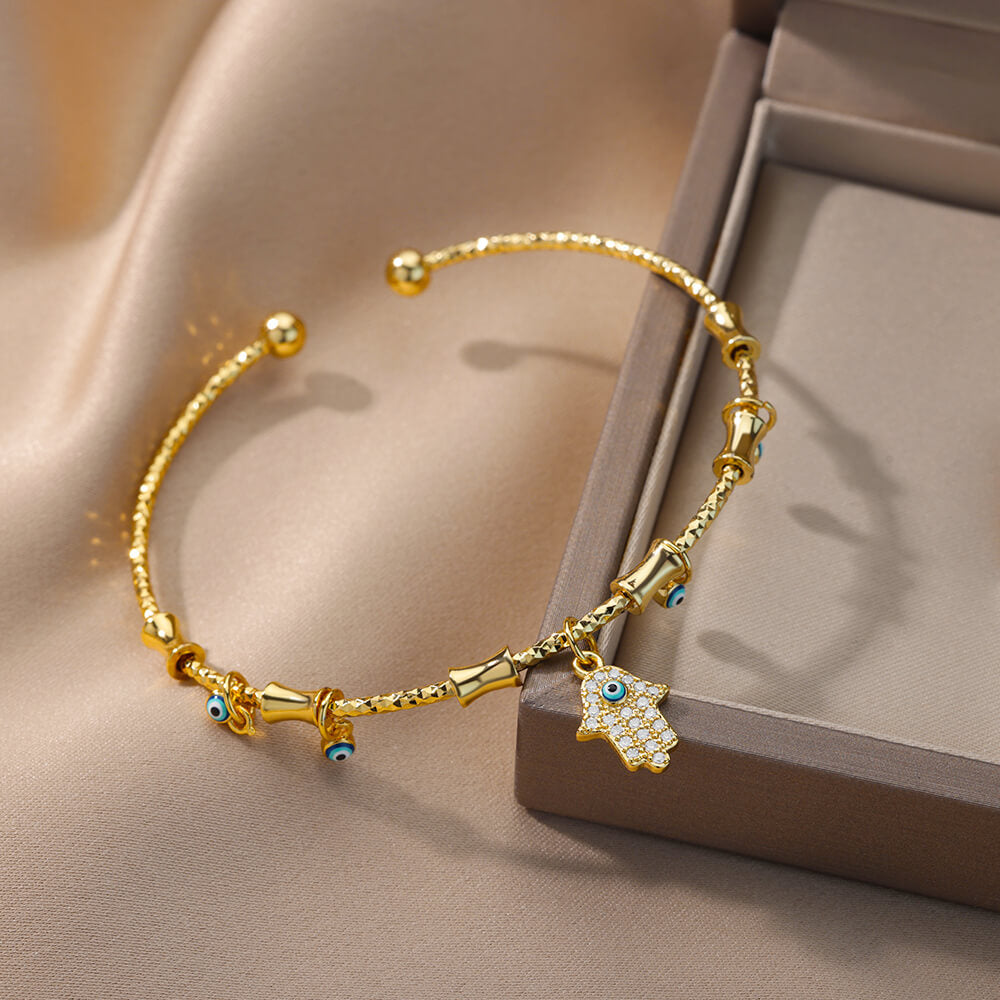 Bracelet jonc doré avec un pendentif main de Fatma serti de zircon, et de plusieurs petits yeux bleus porte-bonheur.