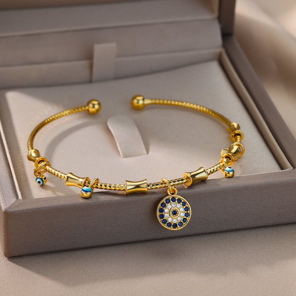 Bracelet jonc doré orné d'un pendentif œil bleu et blanc en zircon, avec des breloques œil bleu tout autour, présenté dans une boîte cadeau.