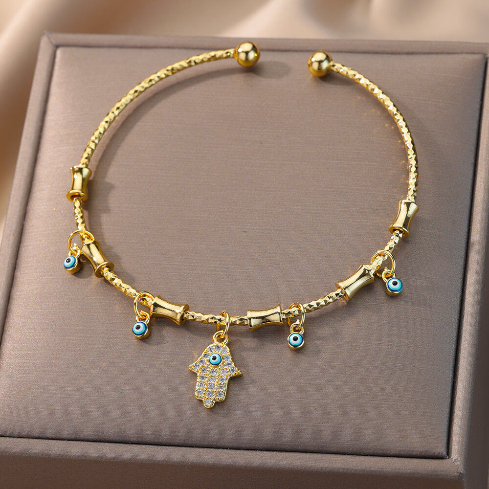 Bracelet jonc doré avec pendentifs main de Fatma et mauvais œil, orné de zircons scintillants.