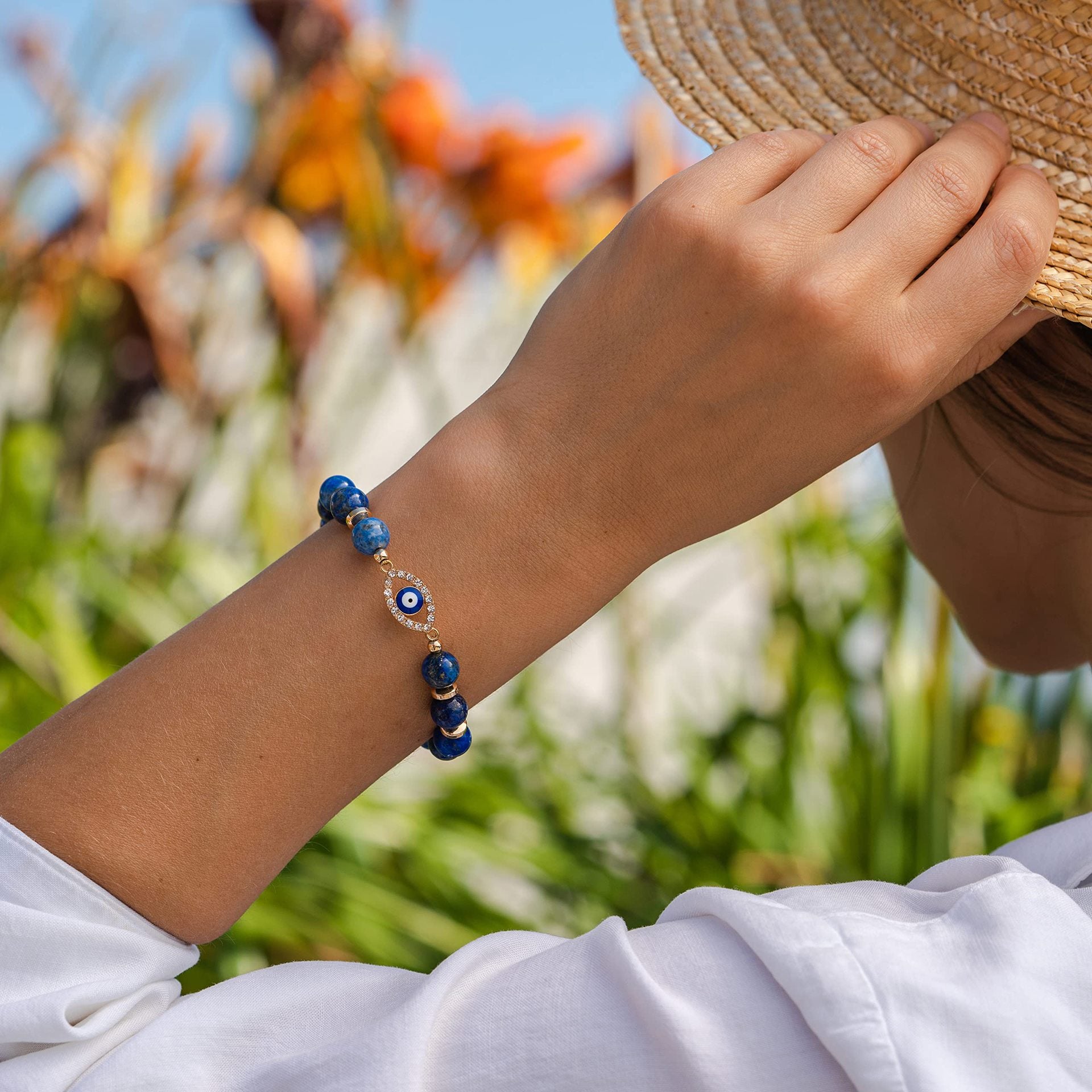 Bracelet en Lapis Lazuli avec un pendentif œil bleu serti de diamants, porté au poignet d'une femme sur fond flou de verdure.
