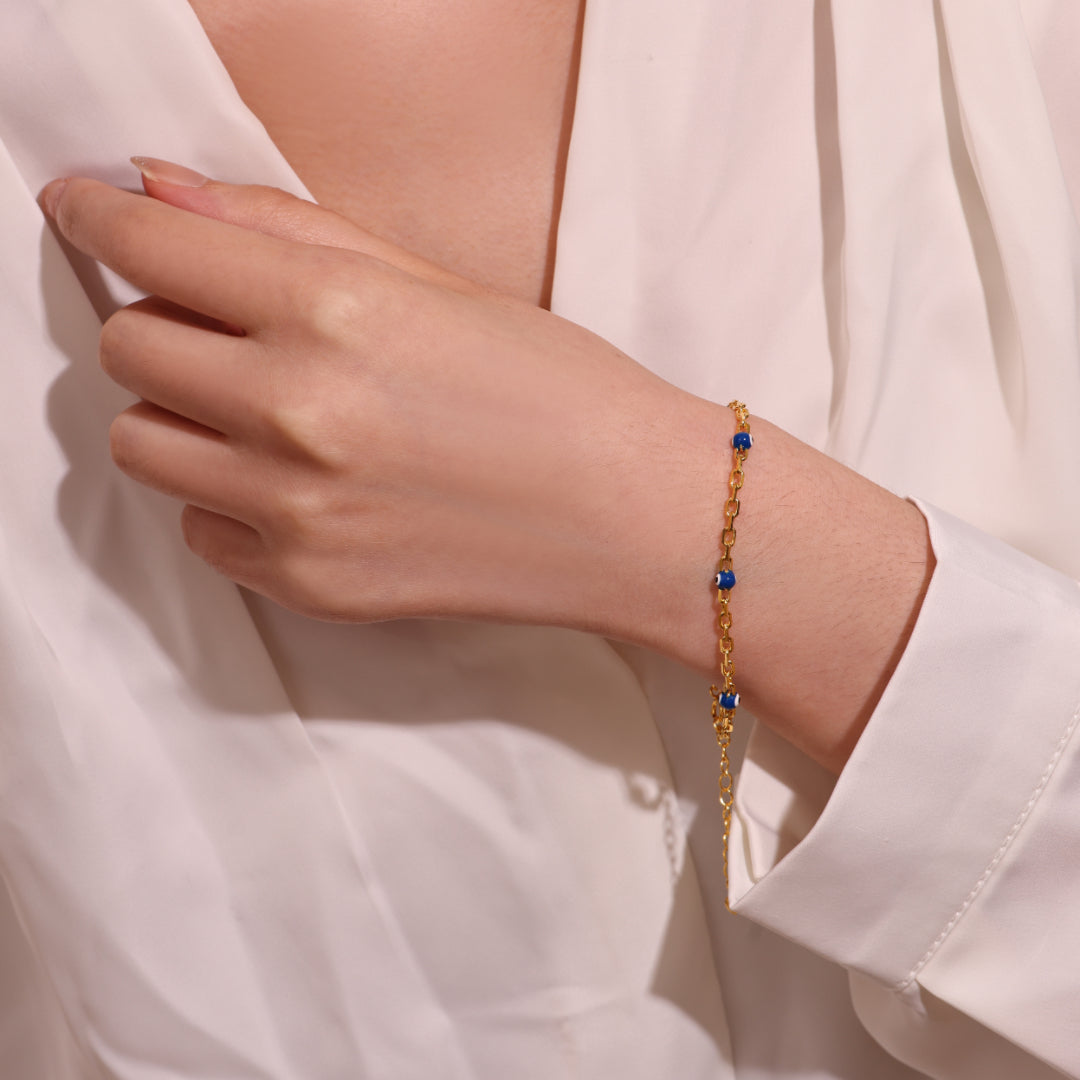 Bracelet fin en argent 925 doré avec des petites perles bleues disposées le long de la chaîne, porté au poignet d'une femme