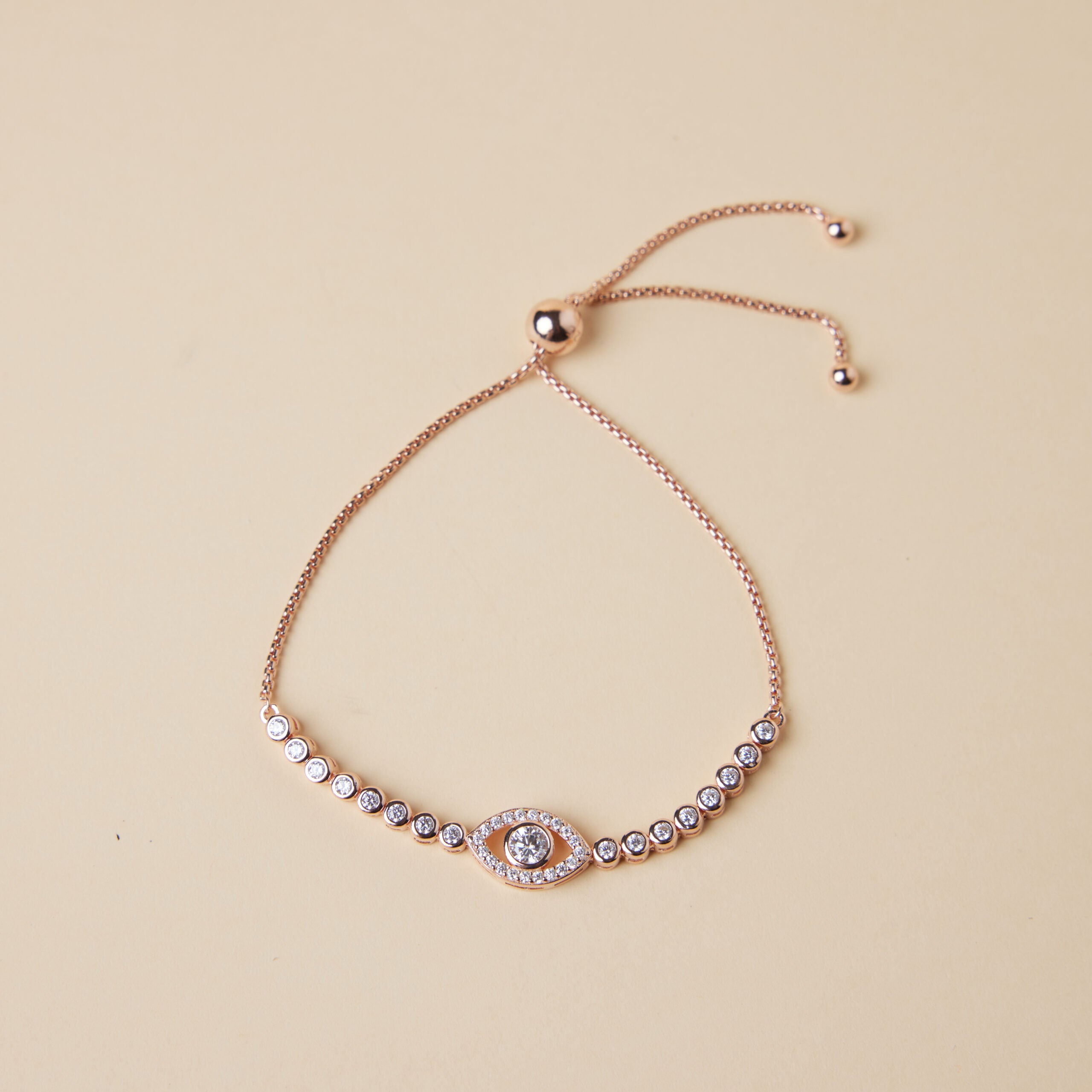 Bracelet œil de protection en argent plaqué or rose, orné de zirconiums scintillants et réglable par une chaîne coulissante.