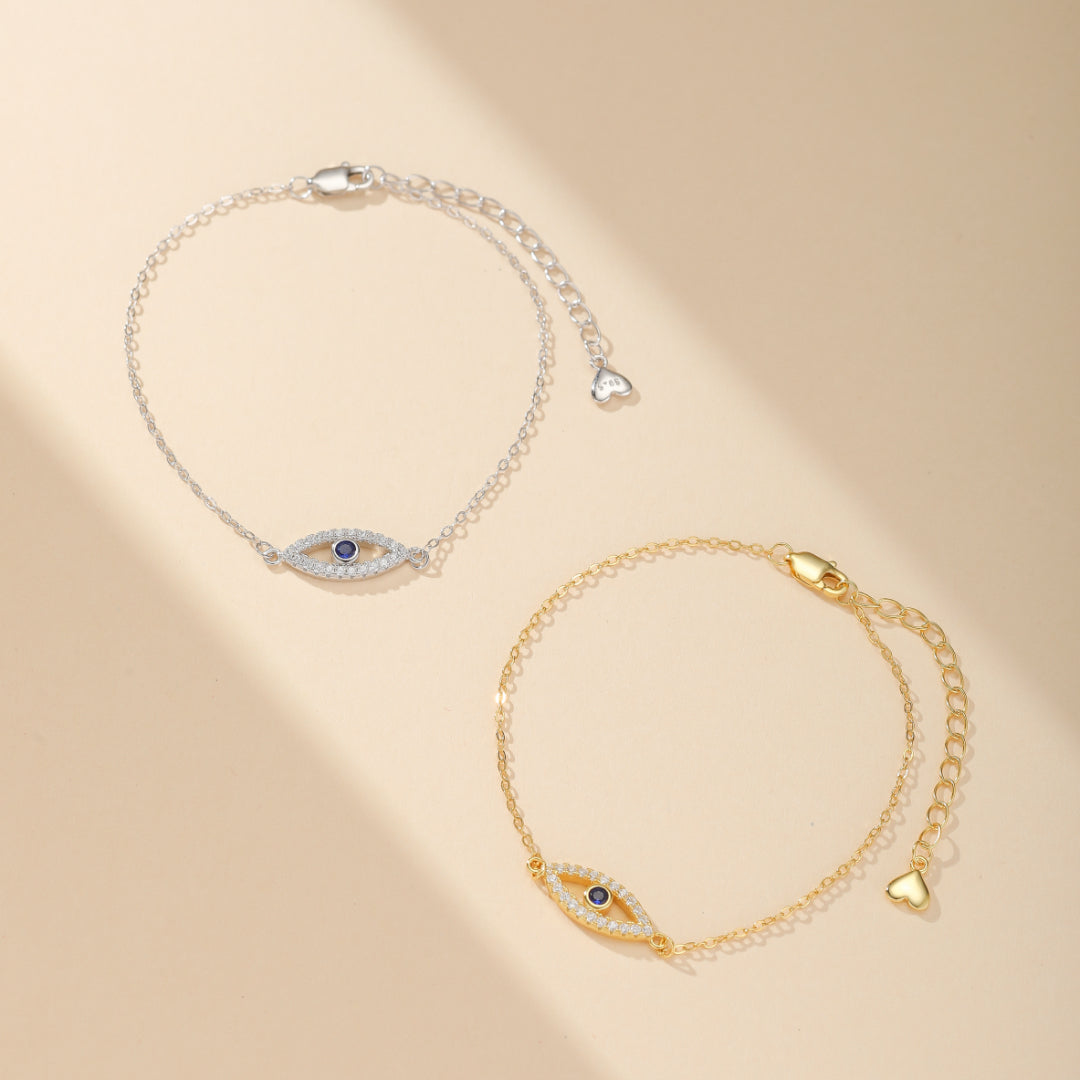 Deux bracelets avec un pendentif en forme d'œil stylisé serti de zirconiums et d'une pierre bleue centrale, l'un en argent 925 et l'autre doré.