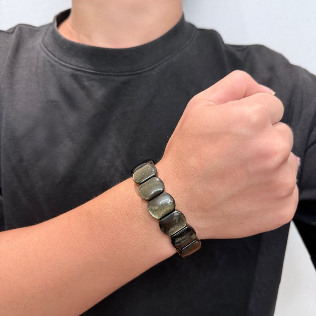 Bracelet en obsidienne dorée aux perles plates sur le poignet d'une personne portant un t-shirt noir