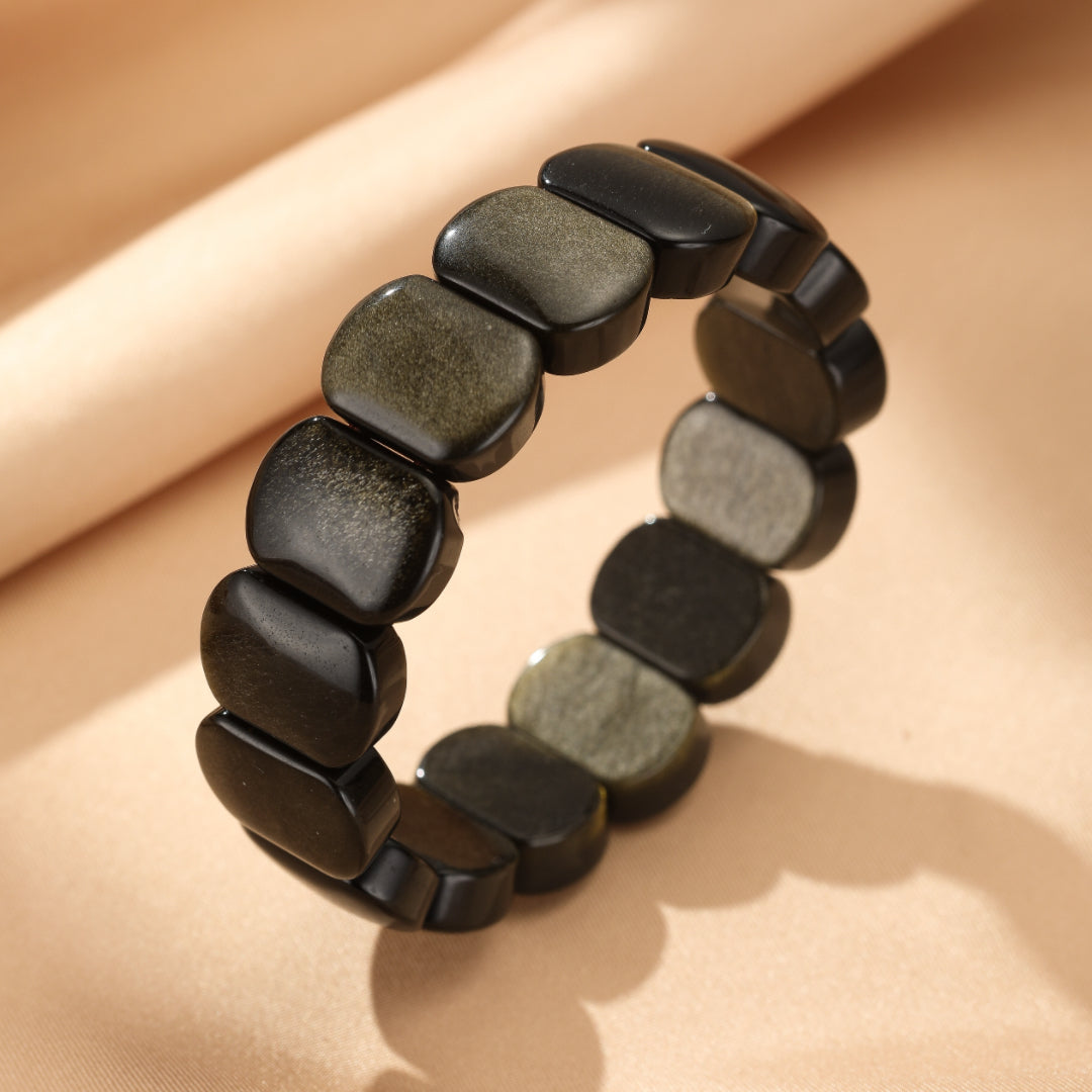 Bracelet fait de pierres d'obsidienne dorée aux reflets verts et noirs, disposées sur une chaîne.
