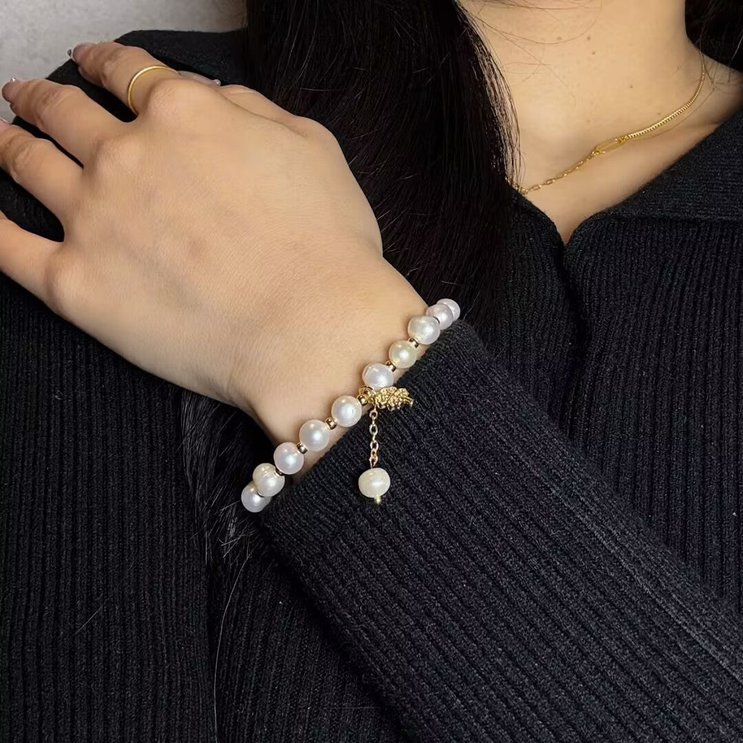 Bracelet en perles d'eau douce avec un pendentif trèfle à quatre feuilles doré et une petite perle suspendue, porté au poignet d'une femme