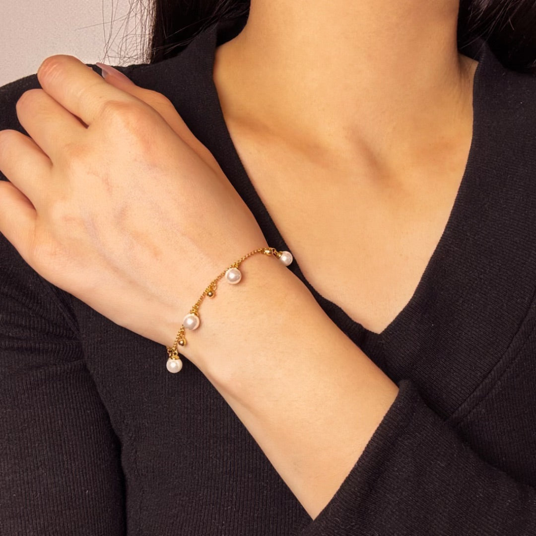 Bracelet fin en argent 925 avec de petites perles blanches et des billes dorées suspendues, porté au poignet d'une femme.