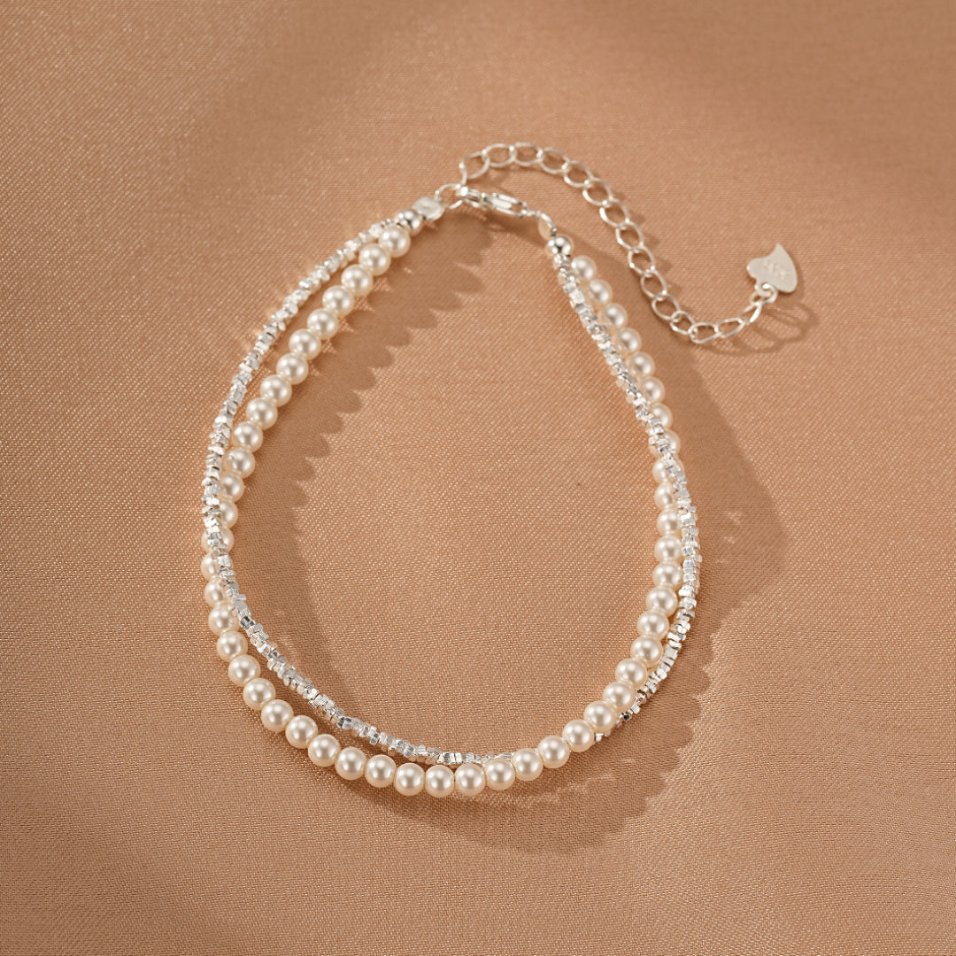 Bracelet double rang avec perles nacrées et chaînette scintillante en argent, orné d'un petit cœur à l'extrémité.