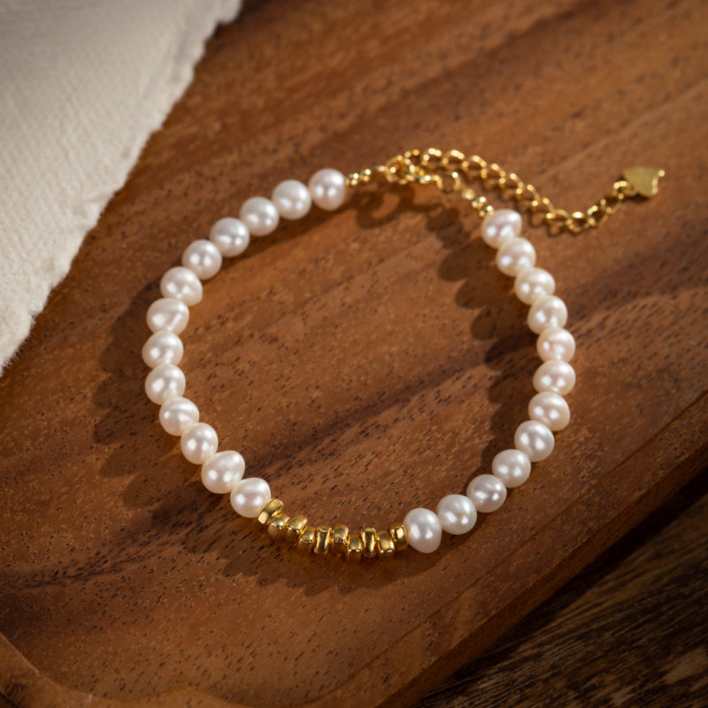 Bracelet en perles blanches naturelles et petites perles dorées, monté sur une chaîne plaquée or ajustable.