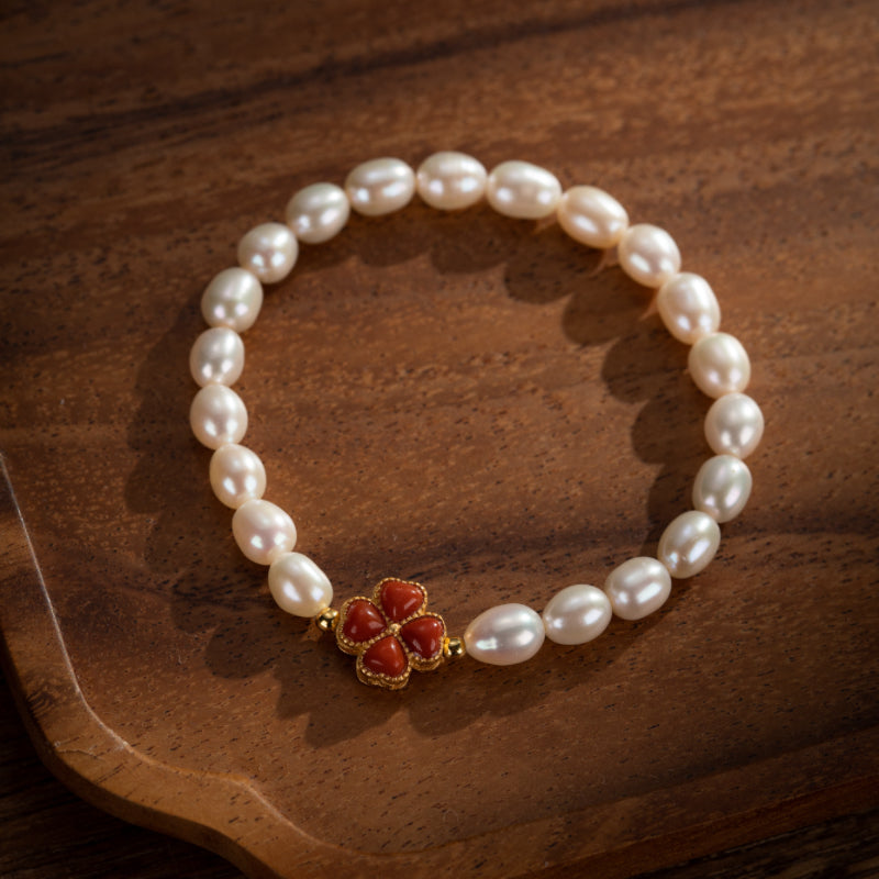 Bracelet en perles d'eau douce avec un charmant trèfle rouge en corail, monté sur un fil doré, sur un fond en bois.