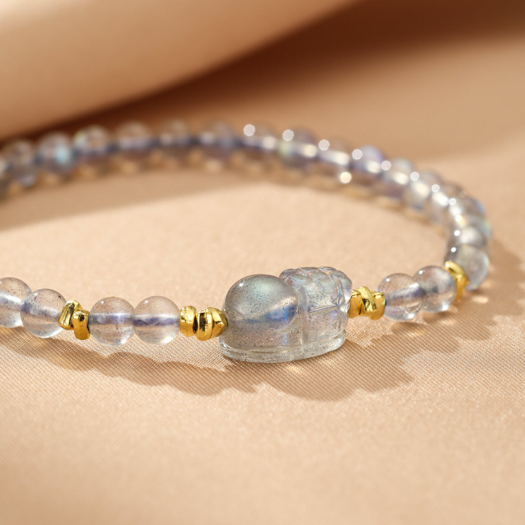 Bracelet en argent plaqué or avec une figurine Pi Xiu sculptée dans une pierre de lune et des perles de labradorite bleues et grises.