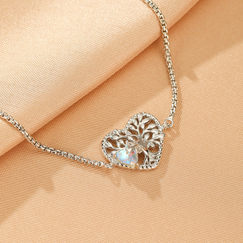 Bracelet en argent avec un pendentif en forme de cœur ajouré représentant l'arbre de vie, orné d'une pierre de lune irisée.