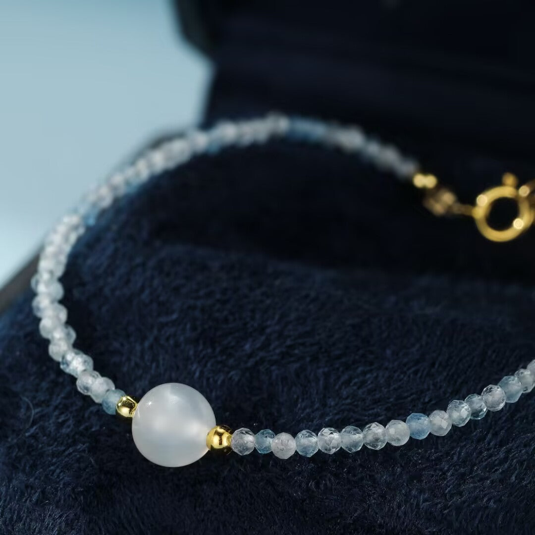 Bracelet Rêverie des Flots en pierre de lune et aigue-marine, orné d'une perle centrale et de petites pierres bleues facetées, avec fermoir doré.