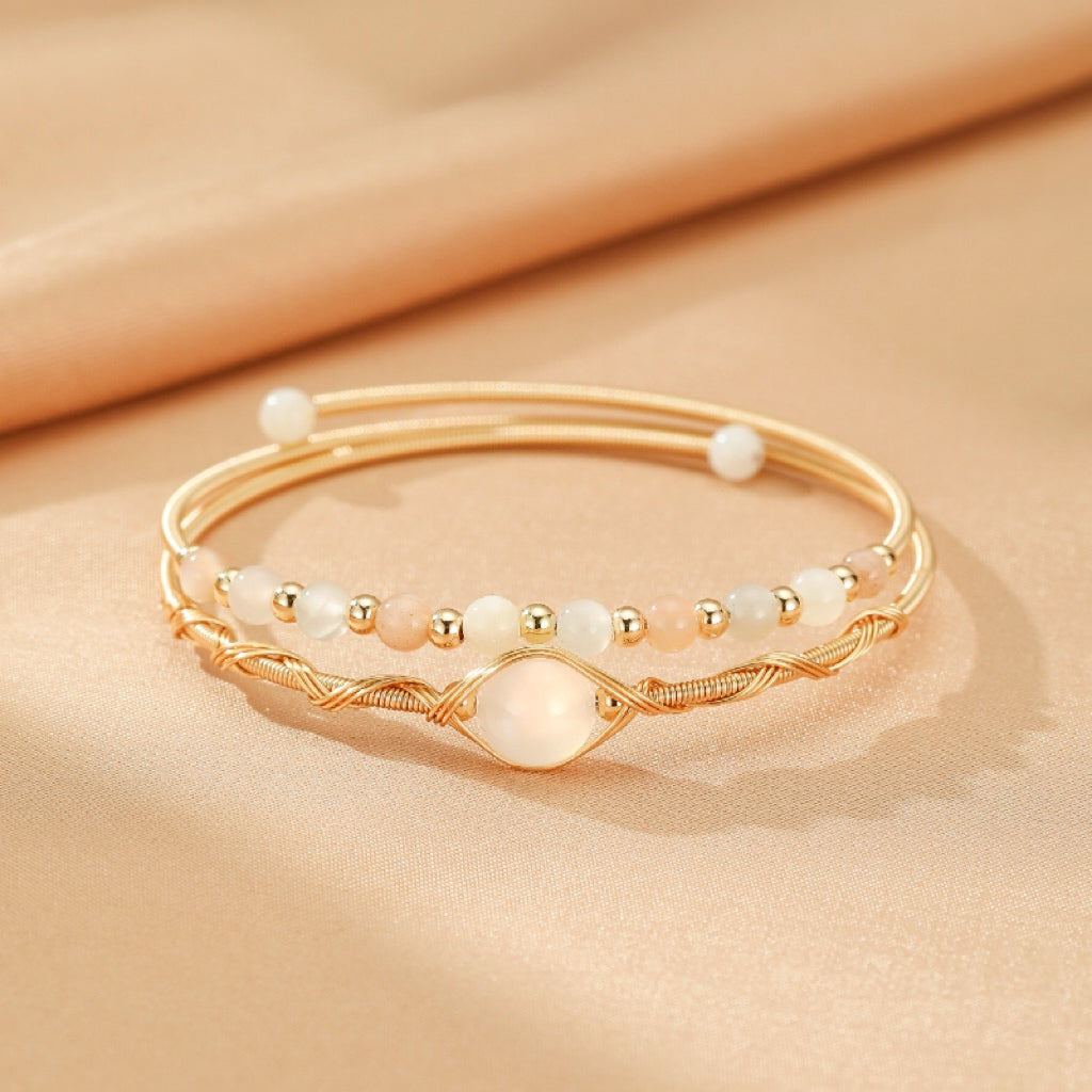 Ensemble de deux bracelets fins en plaqué or 14K, l'un orné de petites perles roses et blanches, l'autre d'une pierre de lune nacrée centrale entourée de fils torsadés.
