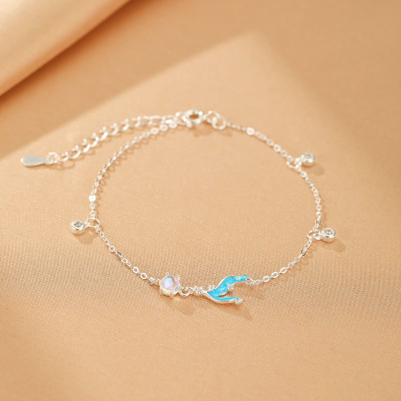 Bracelet en argent fin avec une pierre de lune opalescente et un pendentif queue de sirène bleu vif, orné de petites pierres scintillantes.