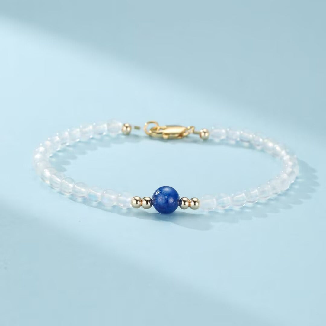 Bracelet fin en pierres de lune translucides avec une perle bleue centrale et des perles dorées, fermoir mousqueton doré.