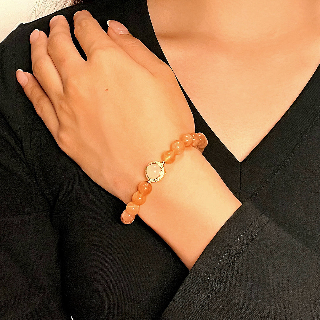 Bracelet fait de perles rondes de pierre de soleil orange et d'une perle centrale plus pâle, monté sur un poignet féminin.