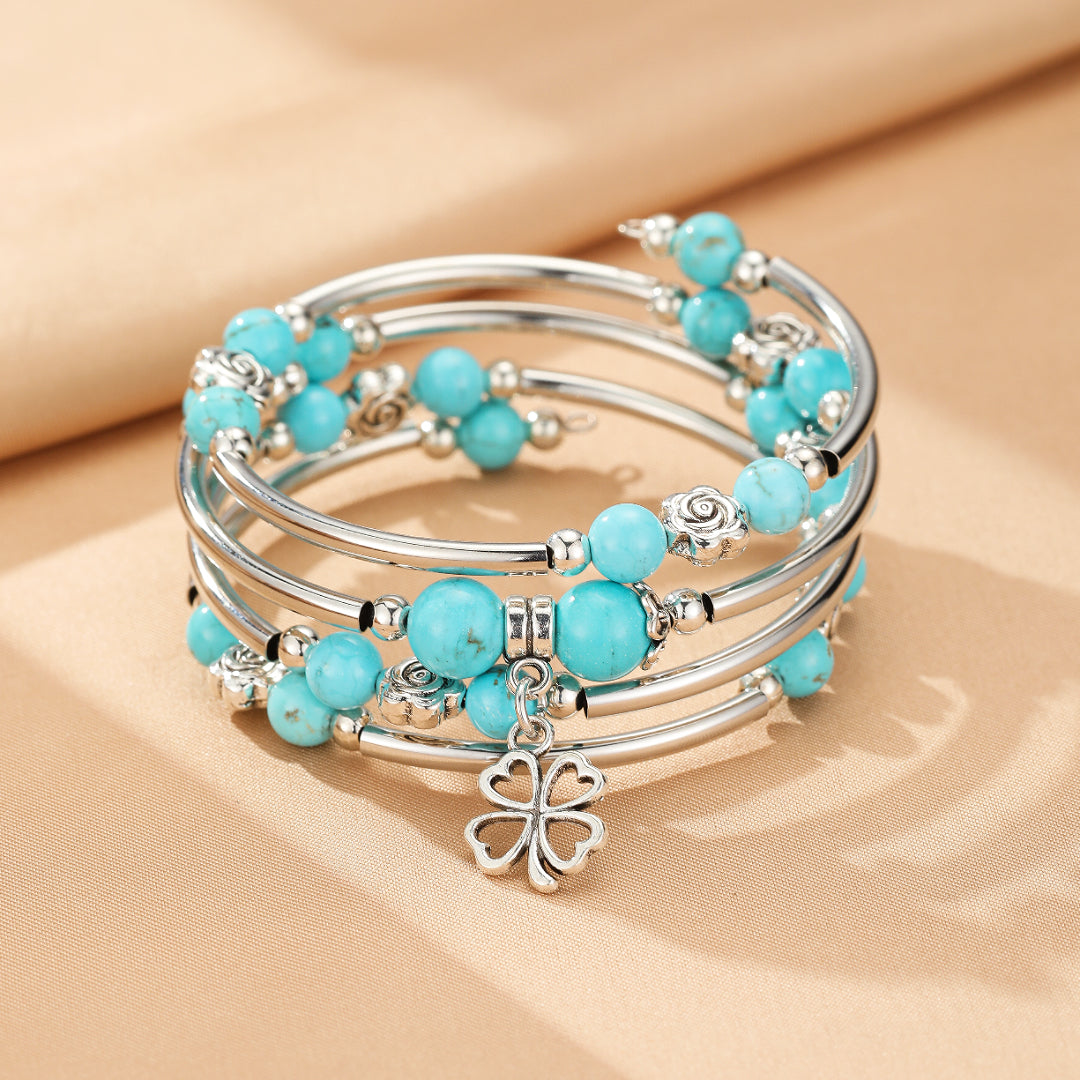 Bracelet jonc enroulé argenté avec des perles turquoise naturelles et un pendentif trèfle à quatre feuilles, rappelant la chance radieuse.
