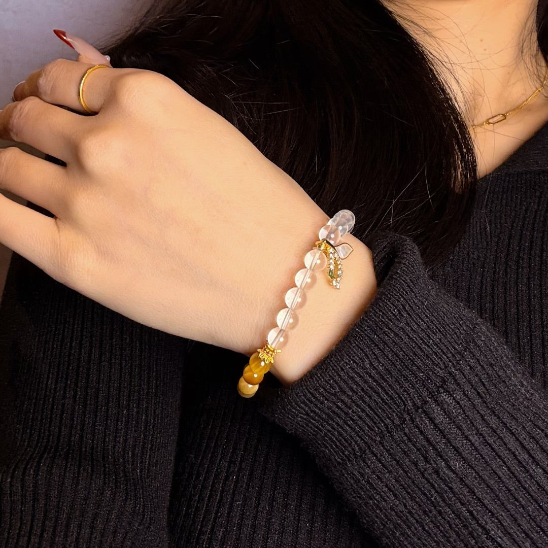 Gros plan sur un bracelet fait main avec des perles en quartz clair et œil de tigre, orné d'un pendentif en forme de papillon.