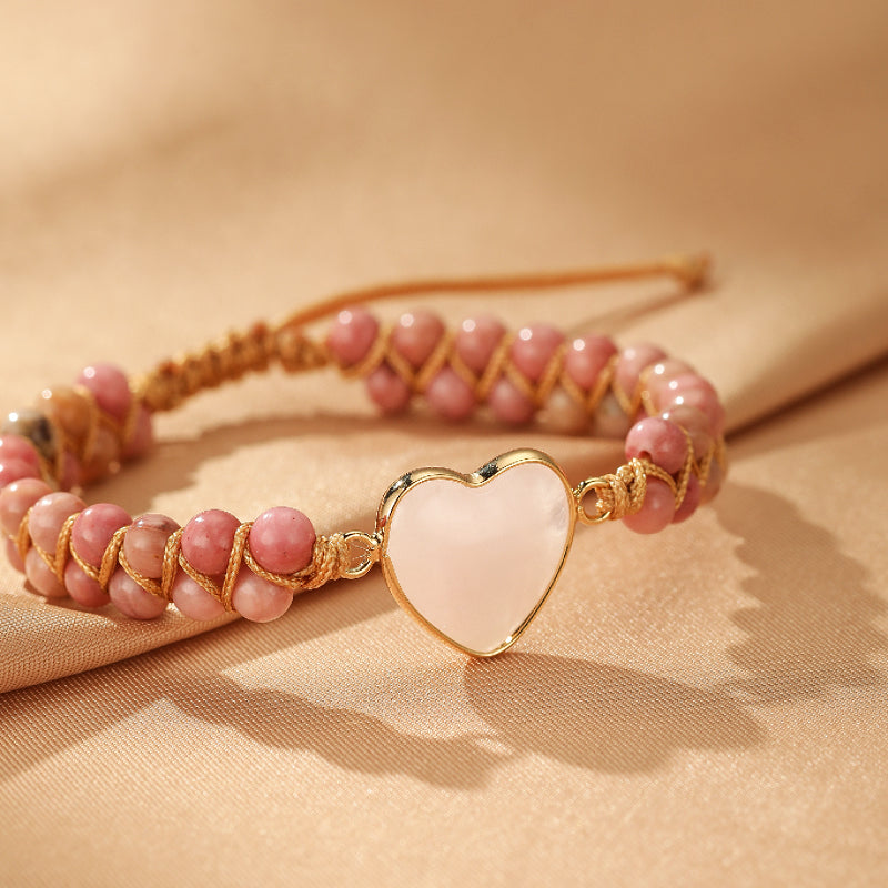 Bracelet "Cœur de Joie" en quartz rose avec un pendentif en forme de cœur en nacre blanche, monté sur un cordon tressé doré.