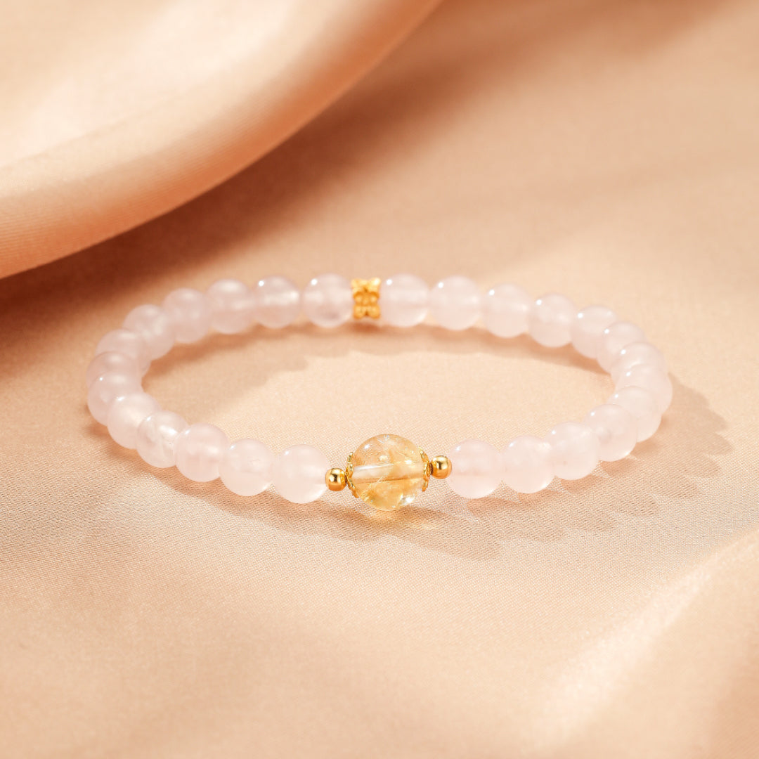 Bracelet élastique en quartz rose avec une perle centrale en citrine facettée et des perles d'espacement plaquées or, sur un fond satiné rose pâle.