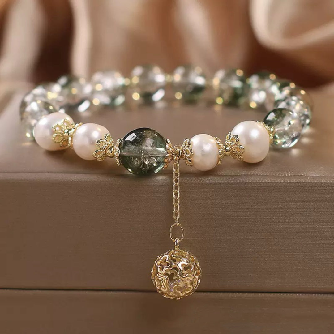 Bracelet élégant avec des perles nacrées et des pierres de quartz vert, agrémenté d'un pendentif sphérique ajouré en or.