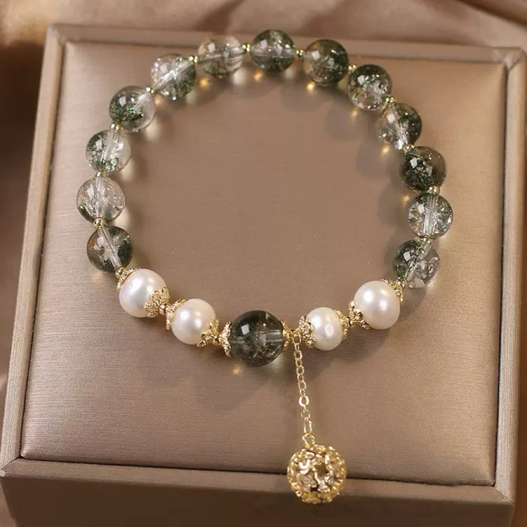 Bracelet élégant fait de perles d'eau douce blanches et de quartz vert inclusions rondes, avec un pendentif boule ajourée dorée.