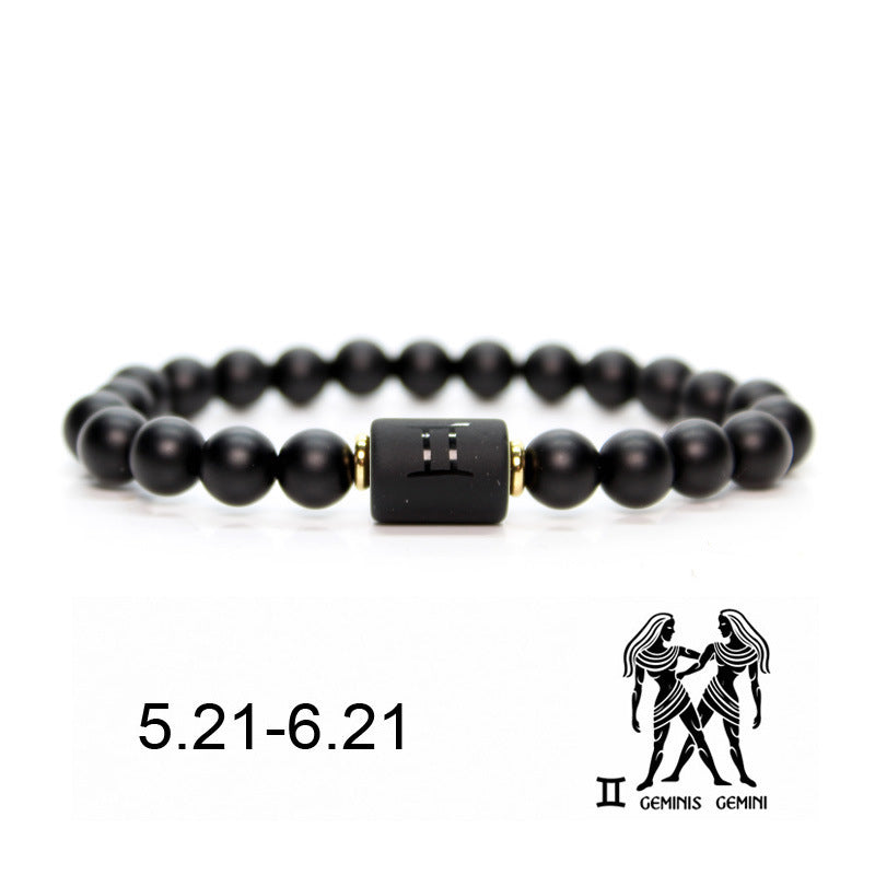 Bracelet en onyx noir avec un pendentif cylindrique noir gravé du signe astrologique Gémeaux et des dates 5.21-6.21. Il est orné de petites perles dorées entre les perles d'onyx.