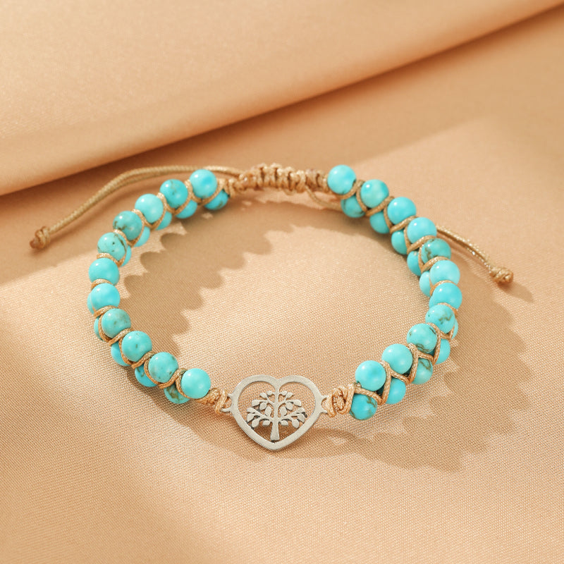 Bracelet en turquoise avec un pendentif en forme de cœur contenant un arbre de vie argenté, monté sur un cordon tressé beige.