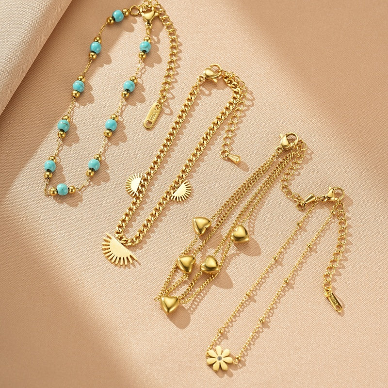 Ensemble de quatre bracelets en or, dont un avec des perles turquoise, un avec des soleils, un avec des cœurs et un avec une fleur.