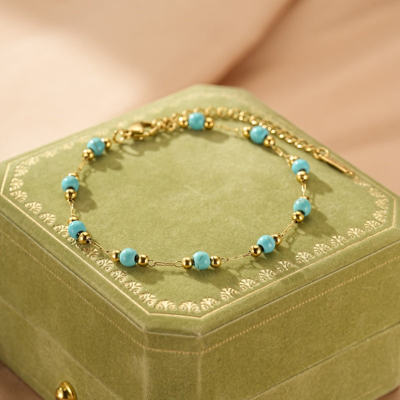 Bracelet fin en or avec des perles turquoise et des petites billes dorées, monté sur une chaîne délicate.