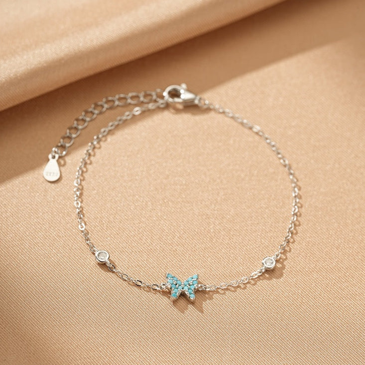 Bracelet fin en argent 925 avec un pendentif papillon incrusté de turquoise et de petits cristaux scintillants.
