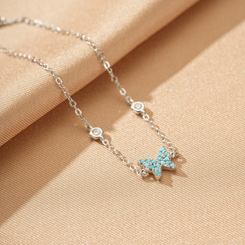 Bracelet en argent avec un pendentif papillon incrusté de turquoise et de petites pierres scintillantes.