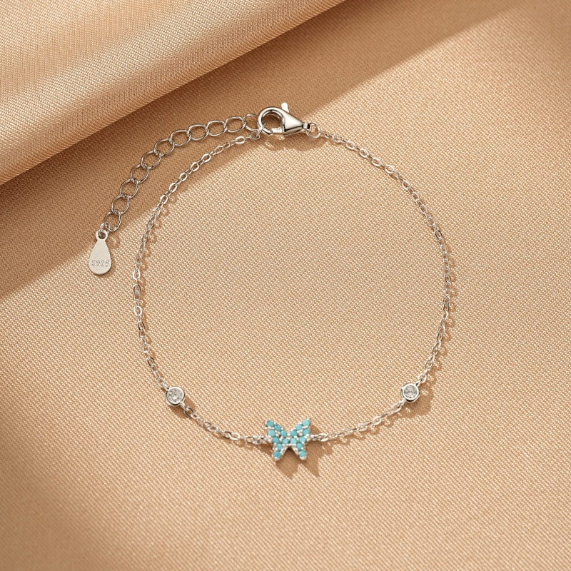 Bracelet en argent 925 avec pendentif papillon bleu turquoise incrusté de zirconias et deux petites pierres rondes scintillantes.