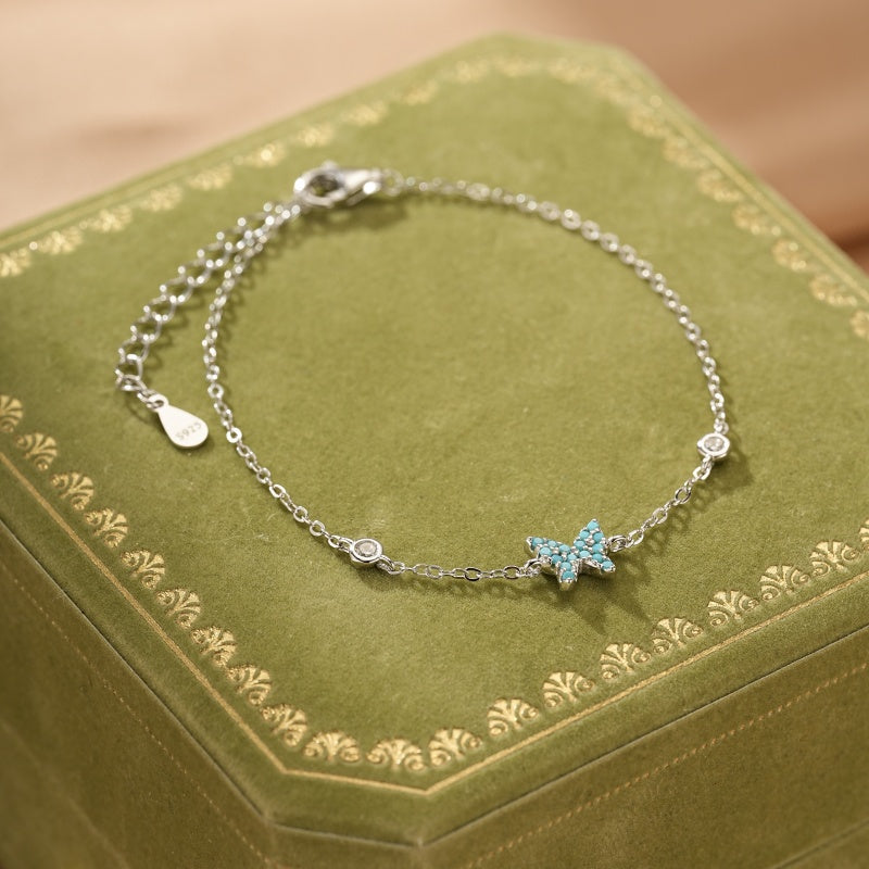 Bracelet en argent 925 avec un pendentif papillon incrusté de turquoise et de petits cristaux scintillants.