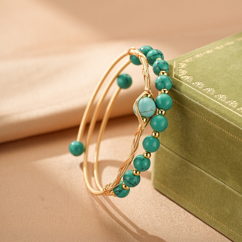 Bracelet jonc doré torsadé serti de perles turquoise et de petites perles dorées, sur un fond neutre.