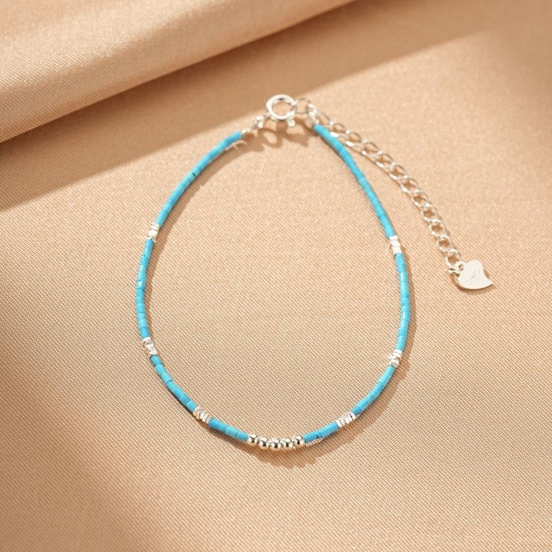 Bracelet fin en argent avec perles turquoise et petits détails argentés, fermoir ajustable avec un pendentif en forme de cœur.