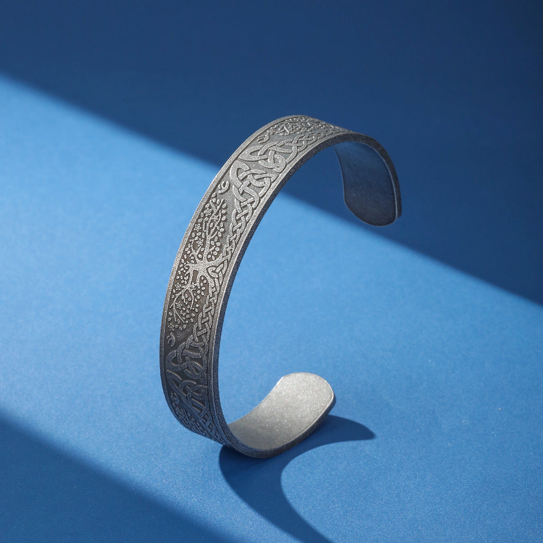 Bracelet Viking Arbre de Vie gravé de motifs celtiques entrelacés et d'un arbre stylisé, en métal argenté sur fond bleu.