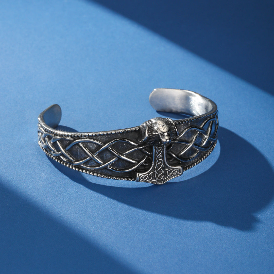 Bracelet jonc viking en argent orné d'un marteau de Thor détaillé et de motifs celtiques complexes, sur fond bleu.