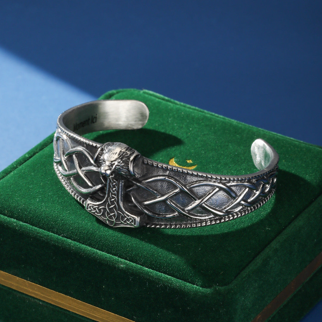 Bracelet jonc viking en argent avec un marteau de Thor stylisé et des motifs celtiques complexes, posé sur un écrin en velours vert.