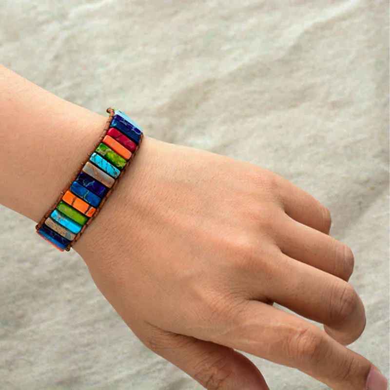 Bracelet jonc torsadé composé de pierres rectangulaires colorées représentant les 7 chakras, sur un fond texturé clair.