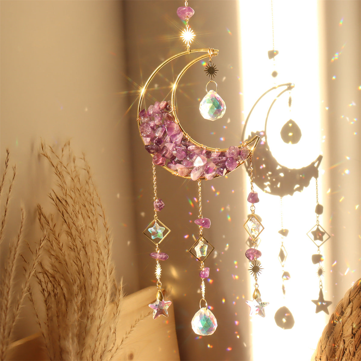 Capteur de soleil artisanal en forme de croissant de lune dorée rempli de petites pierres d'améthyste violettes, orné de cristaux en forme d'étoile et de diamants, avec un prisme suspendu créant des reflets arc-en-ciel.