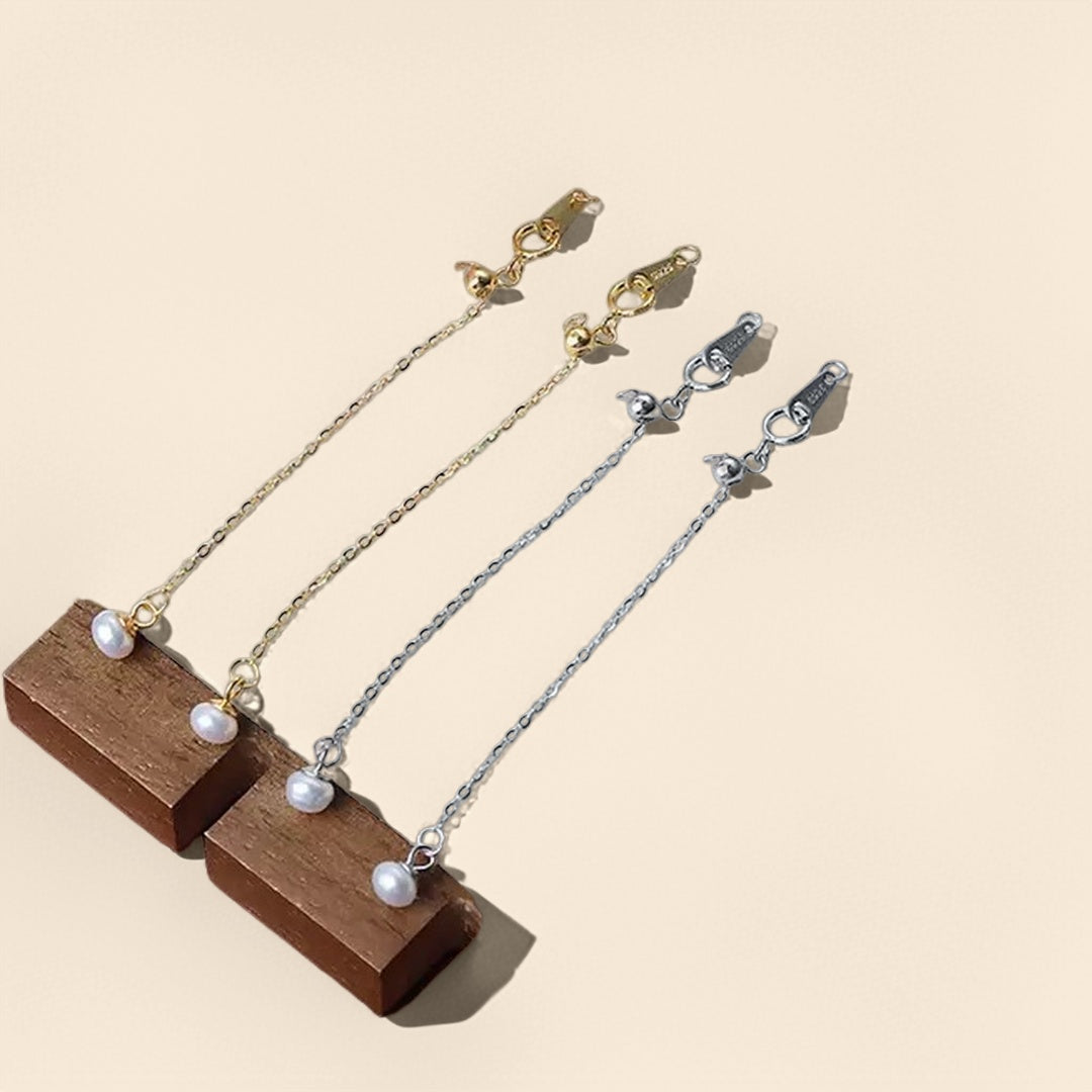 Chaînettes d'extension plaquées argent et or avec une petite perle blanche suspendue, posées sur des blocs de bois.
