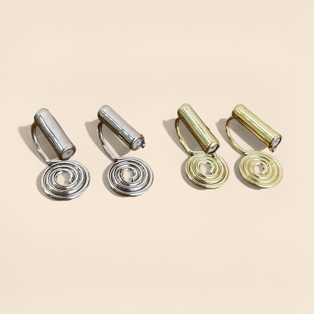 Deux paires de clips d'oreilles argentés et dorés en forme de spirale élégante, présentés sur un fond beige.