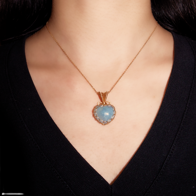 Collier Cœur Océanique avec un pendentif en forme de cœur en aigue-marine, monté sur une chaîne dorée et porté par une femme.