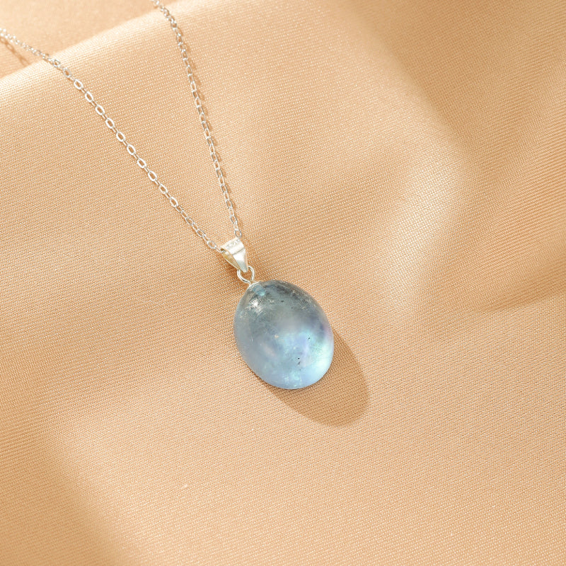 Collier en argent avec un pendentif ovale en aigue-marine bleu pâle, sur un fond texturé beige.