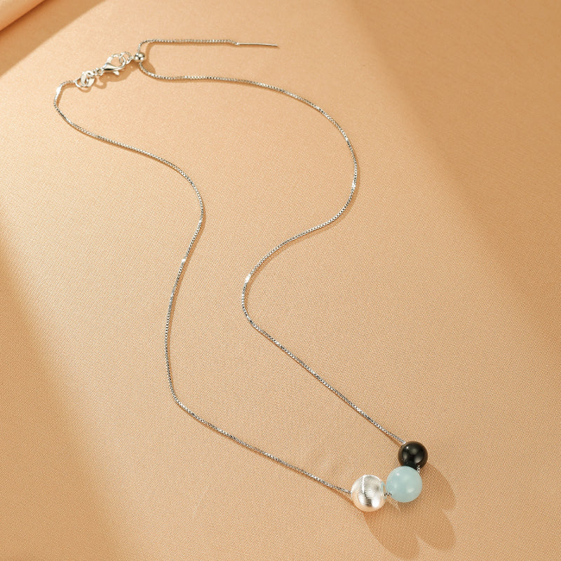 Collier en argent 925 avec une chaîne fine et trois perles rondes : une perle argentée texturée, une perle bleu pâle d'aigue-marine et une perle noire d'obsidienne.