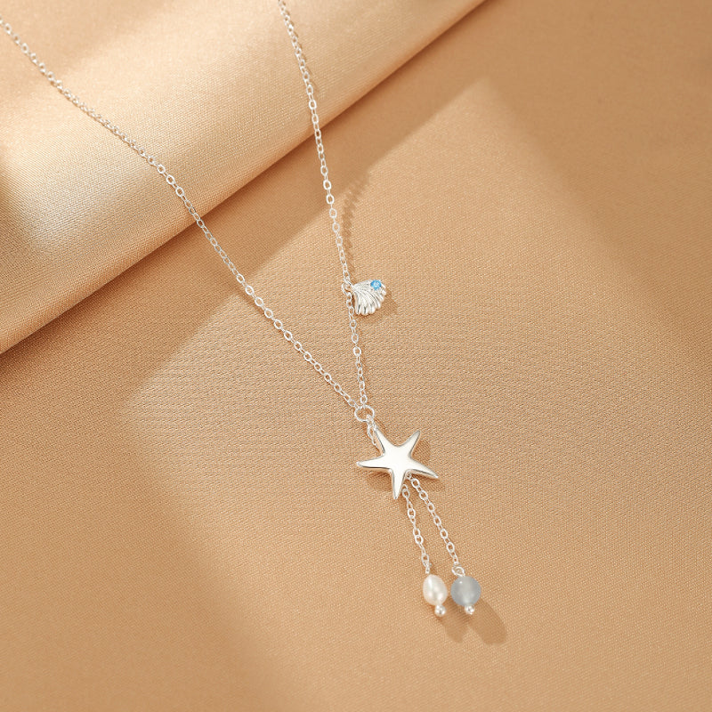 Collier en argent 925 avec pendentif étoile de mer, perle et pierre bleue sur fond beige.